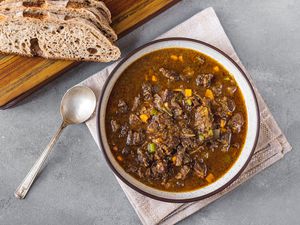 Oxtail soup in a bowl with a spoon and bread slices alongside