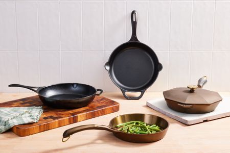 Assortment of cast iron skillets we recommend displayed on cutting boards and a wooden surface against a tiled background 