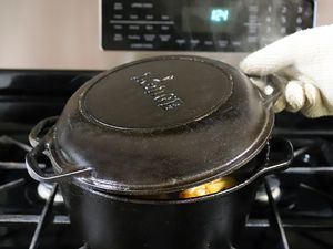 A hand in an oven mitt lifting the lid of Lodge Cast Iron Double Dutch Oven containing food