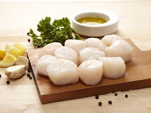 Raw scallops on a cutting board with lemon, garlic, parsley, and olive oil