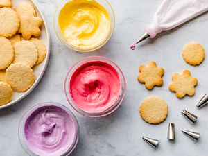 Royal icing in different colors in bowls alongside cookies and decorating tools