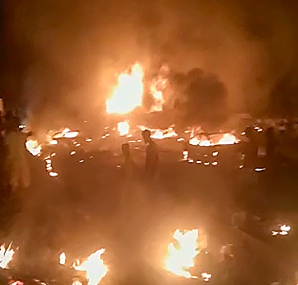 People walking through the devastation as cars burn