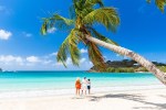 Two parents with one child hugging on palm fringed beach in summer, Antigua, Leeward Islands, Caribbean, West Indies