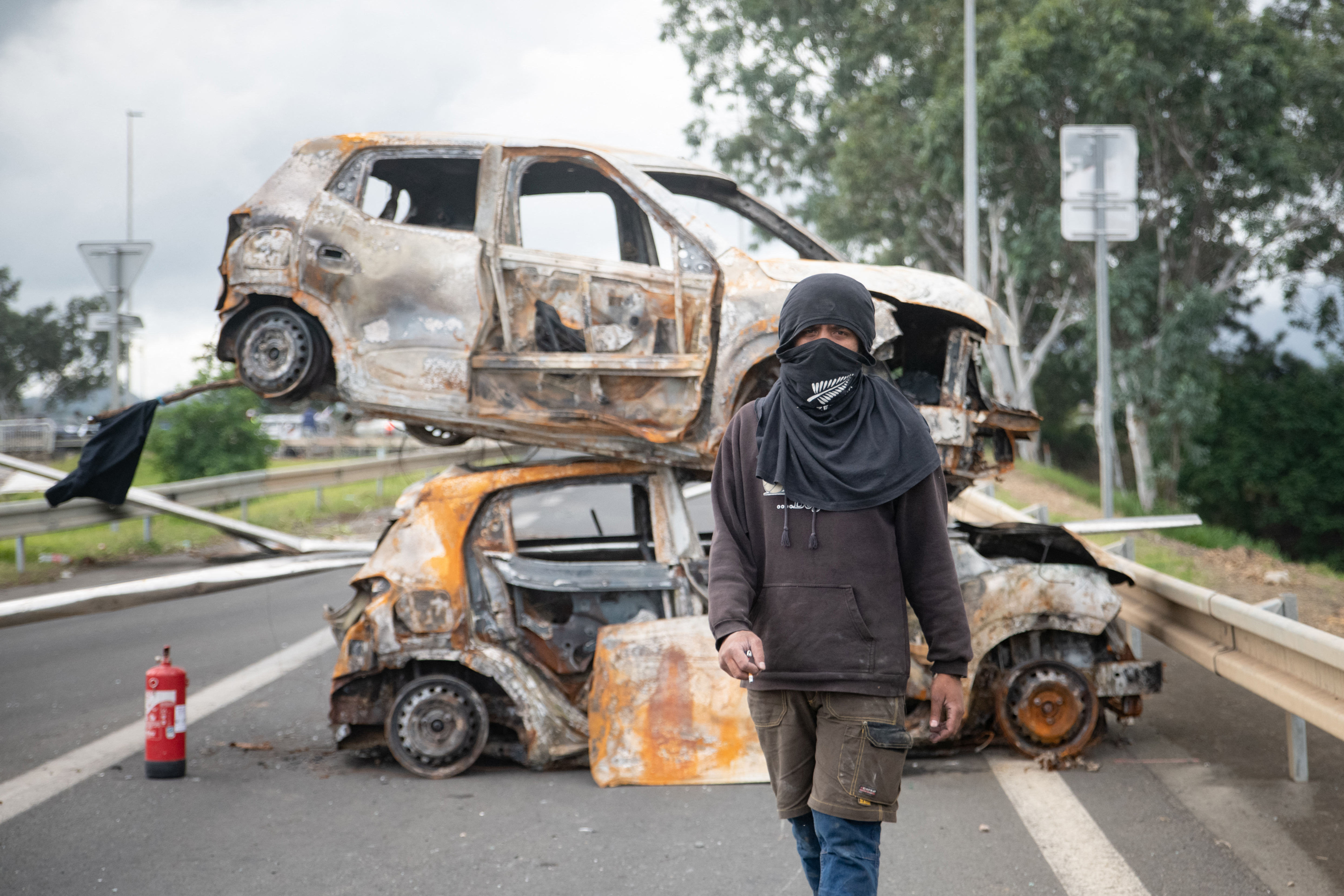 Burnt vehicles block a road at the entrance to Ducos in New Caledonia