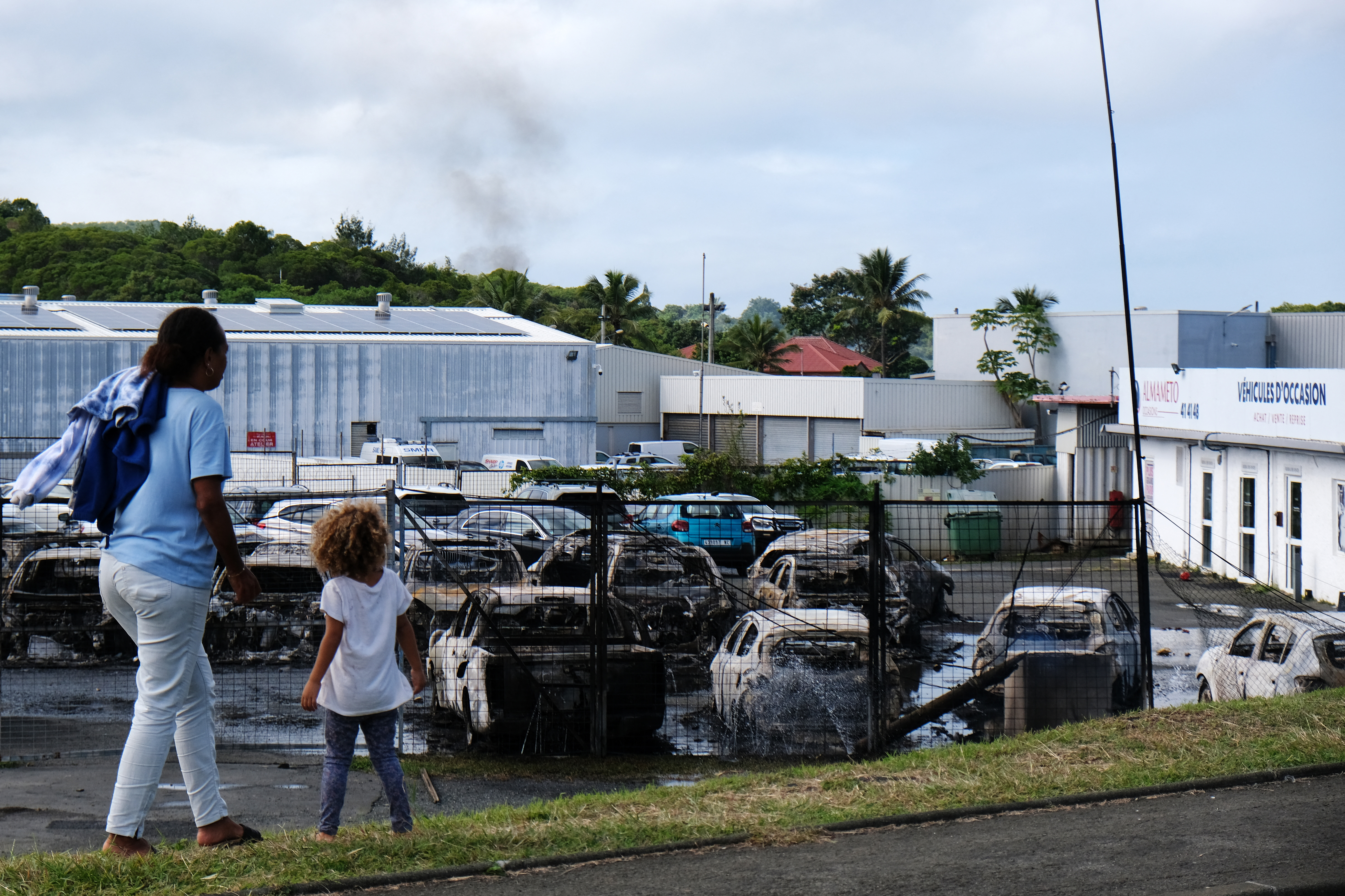 Residents look at burnt cars at a car dealer store in the Belle-Vie district in Noumea