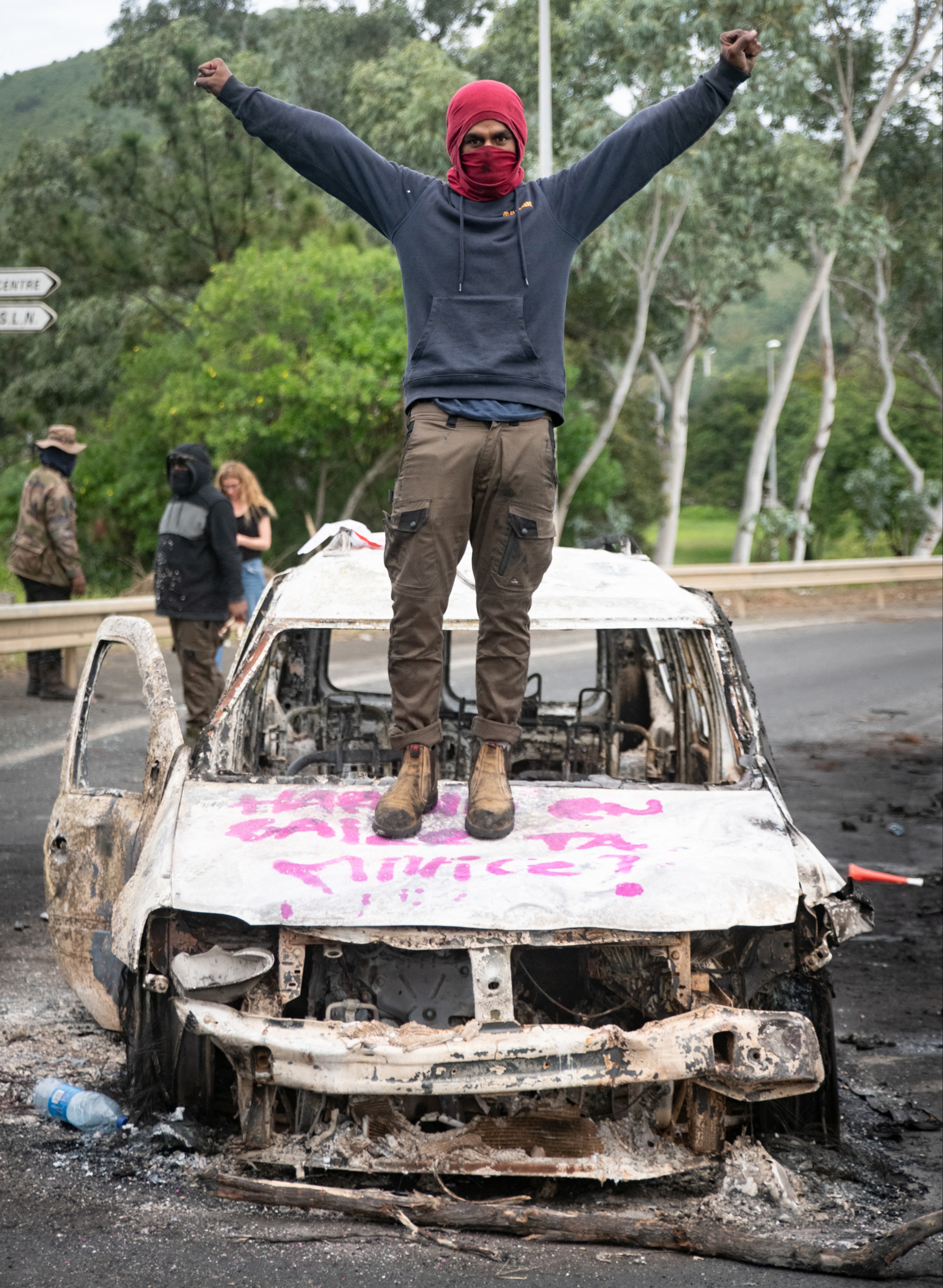 An activist stands atop a burnt car in the territory