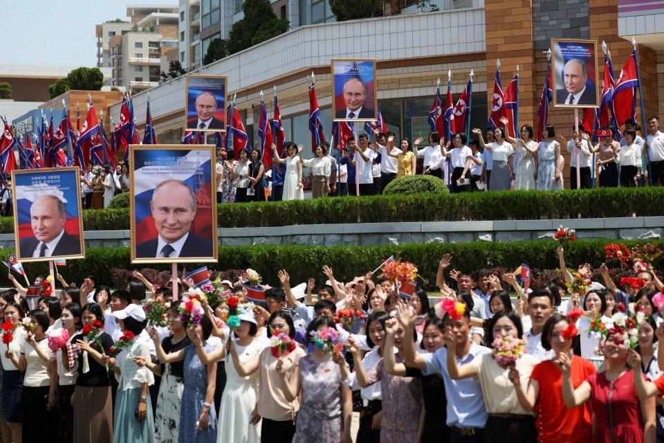 North Koreans waving flowers and holding up portraits of Putin as a motorcade passes in Pyongyang