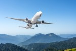 a plane is flying over a mountain range with trees in the foreground