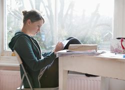 Sixteen year old girl studying and writing notes next to window