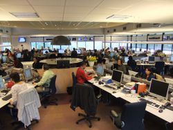 Active newsroom filled with people and equipment.