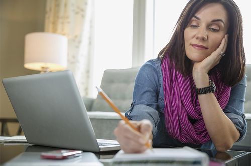 woman with laptop writing in book at table