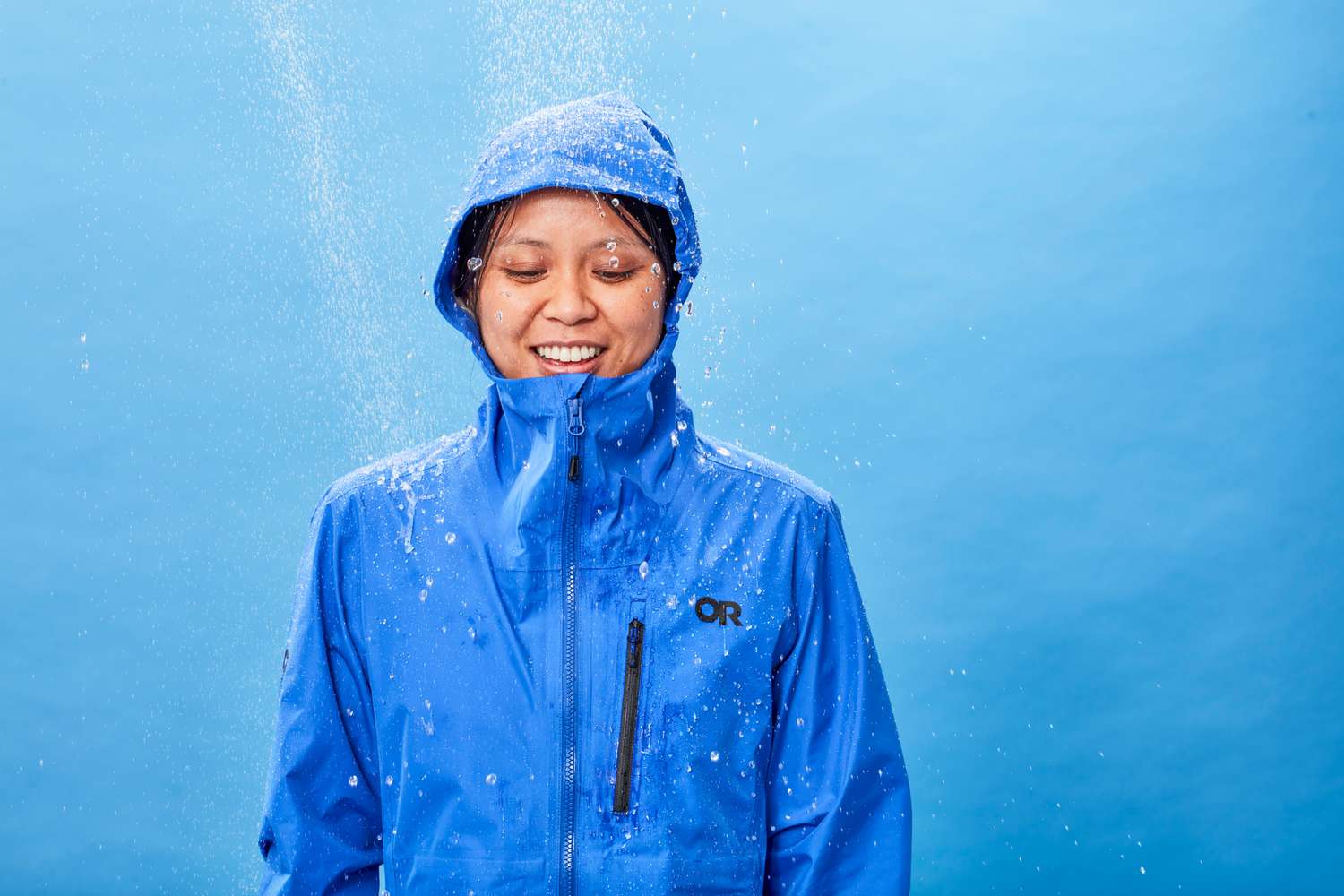 A person standing under a stimulated shower while wearing the Outdoor Research Women's Aspire Super Stretch Jacket