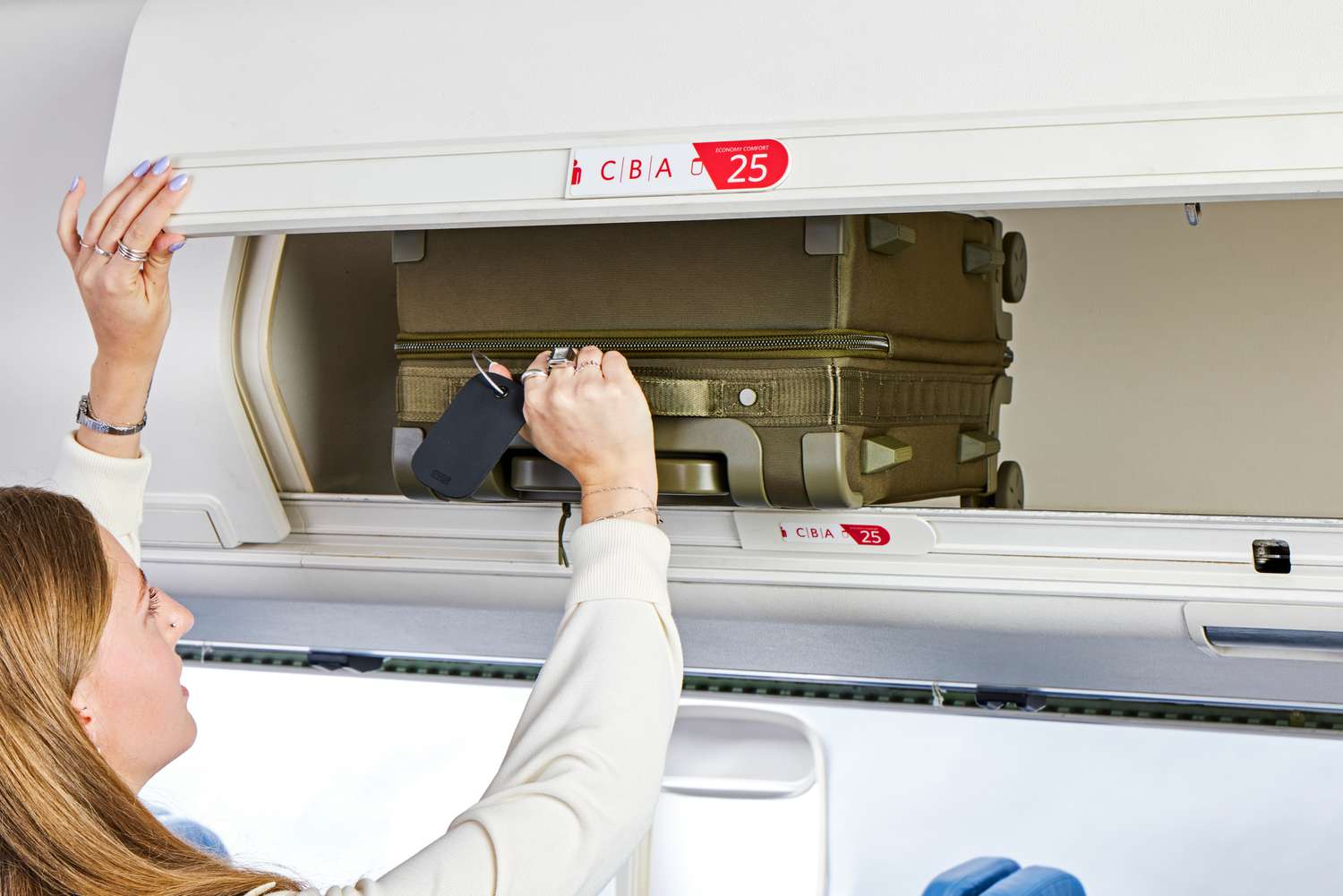 A person placing the Dagne Doverr Seattle Carry On Rolling Luggage 20.5" into an overhead bin