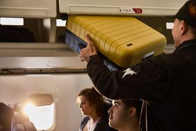 A man puts up a yellow carryon bag in an overhead bin