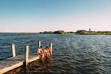 Siblings dipping feet in water on pier at Outer Banks, North Carolina