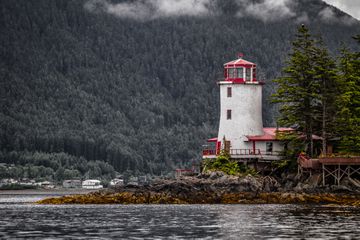 The Rockwell lighthouse against a mountain of pine trees in Sitka, Alaska.