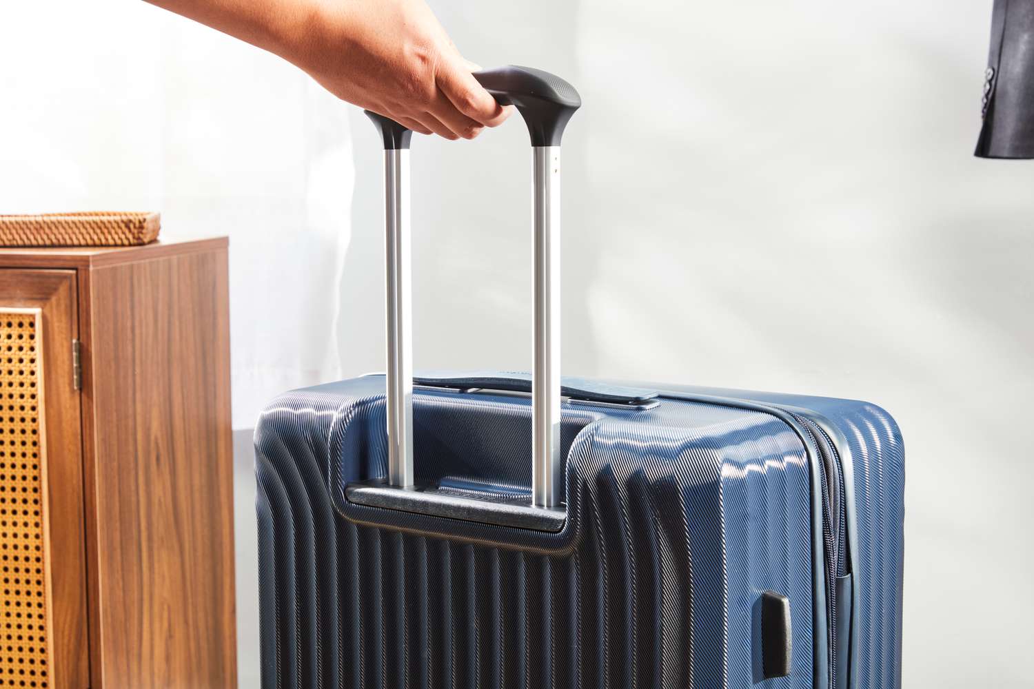 A hand holding the handle on the Travelpro Maxlite Air Medium Check-In Hardside Spinner