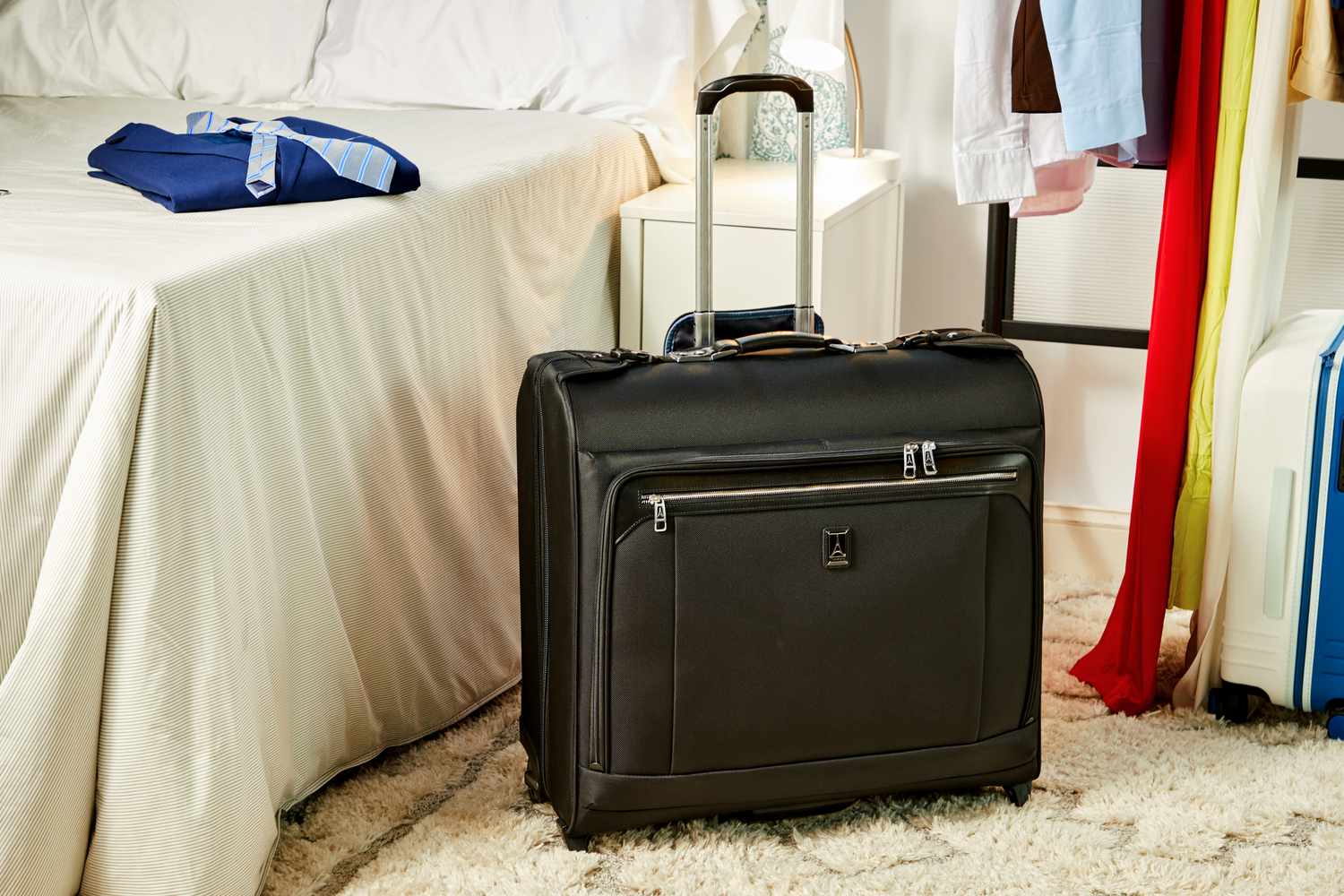 The Travelpro Platinum Elite Check-In Rolling Garment Bag placed on the ground next to a bed