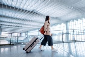 Side view of woman carrying suitcase walking in airport terminal