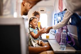 Flight attendant serving food and drinks to family with young kids on an airplane during flight