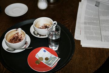 Image of empty coffee drinks and a newspaper on a cafe table with a tip in EU currency