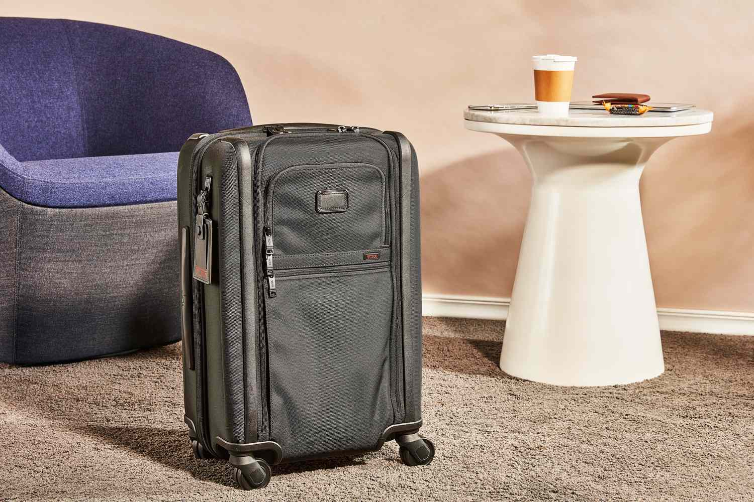 Tumi Alpha International Dual Access 4 Wheeled Carry-On on a rug next to a chair and table