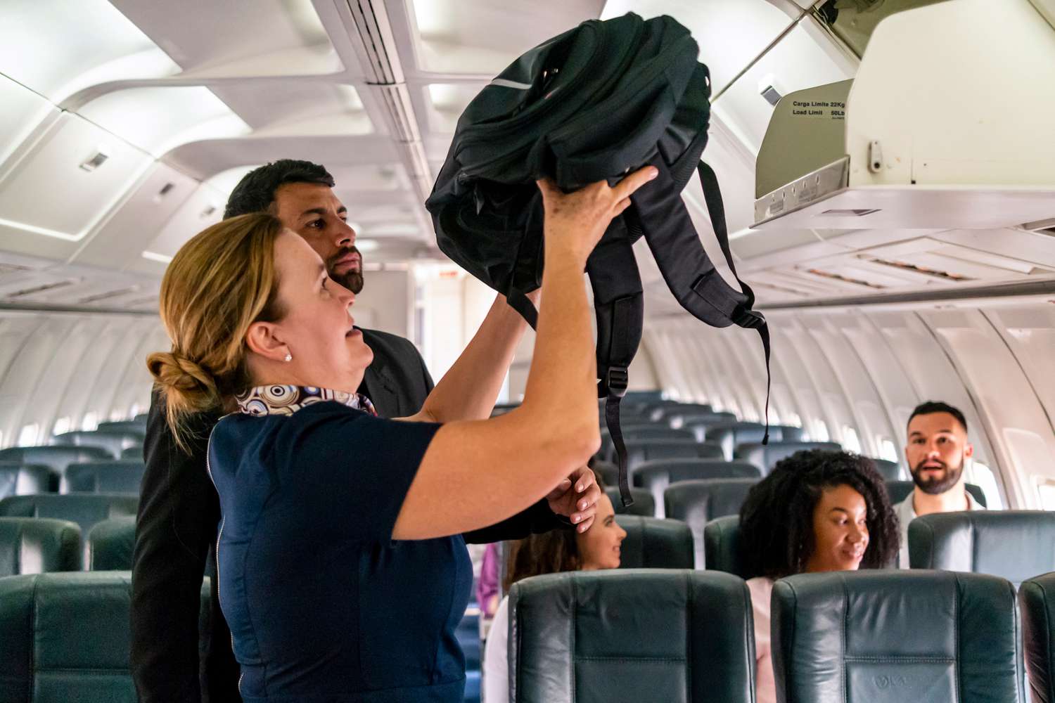 Flight attendant assists passenger with bag in overhead bin 