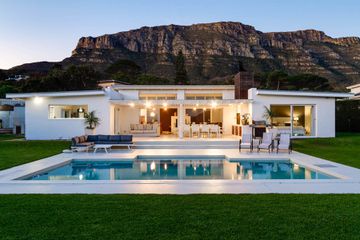 Exterior view of back of white single story mod home and swimming pool with Table Mountain in the background