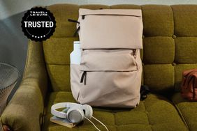 The Everlane The ReNew Transit Backpack displayed on a brown couch next to a pair of headphones and a small bag