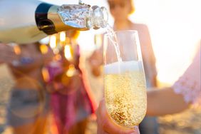 Pouring a glass of champagne with people partying in the background.