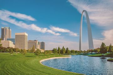 The Gateway Arch National Park is alive with autumn color and green evergreen trees surrounding the lake under the Arch.