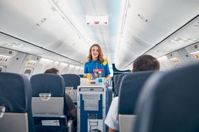 Interior of international airplane with passengers on seats and stewardess in uniform walking the aisle with a drink cart