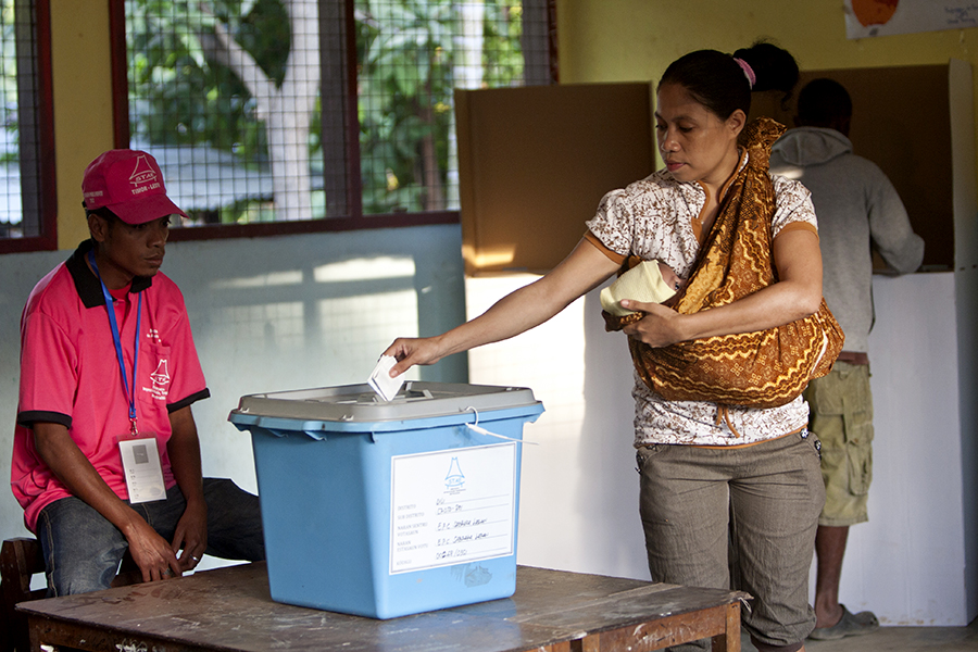 A woman carrying a baby puts her ballot inside a box.