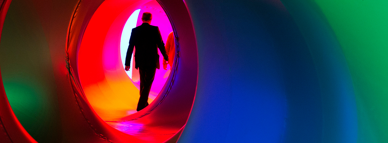 Una foto al estilo de James Bond de un hombre caminando a través de una escultura multicolor que se asemeja a la apertura de una cámara.