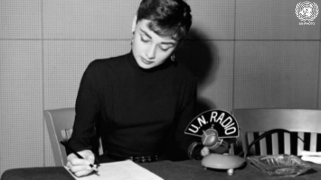 Audrey Hepburn está sentada en un escritorio con lápiz y papel y un micrófono de Radio ONU.