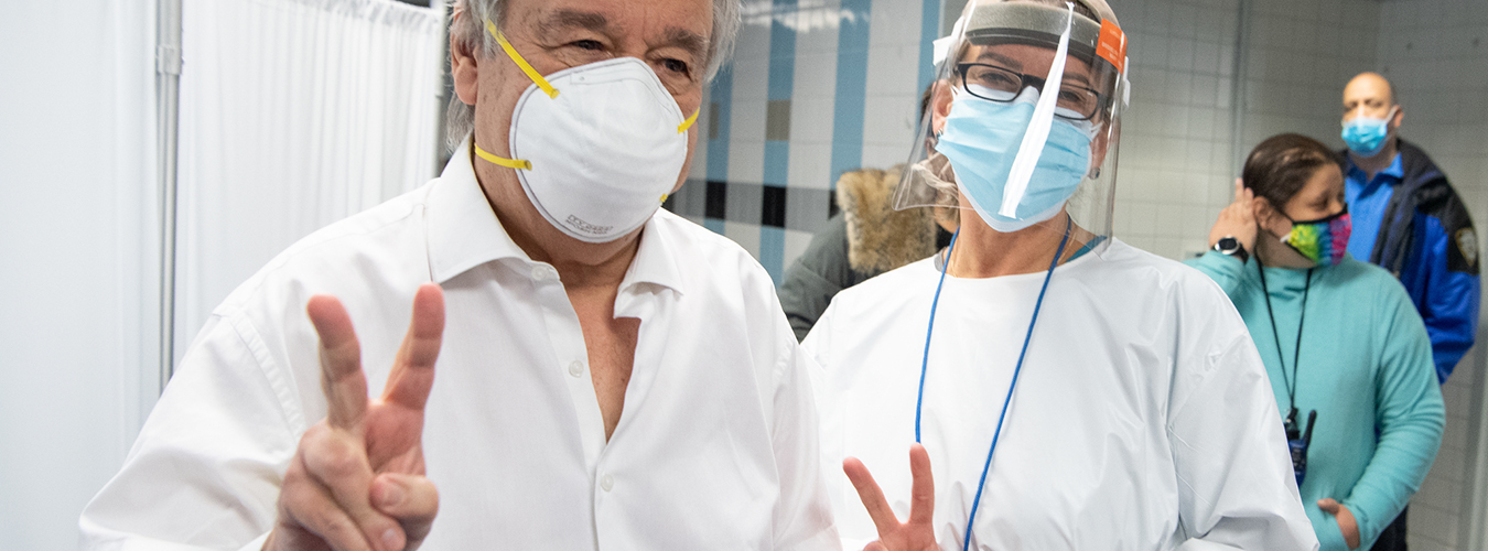 El Secretario General António Guterres y una enfermera llevan máscaras y ambos dan la señal de victoria dentro de un entorno médico.
