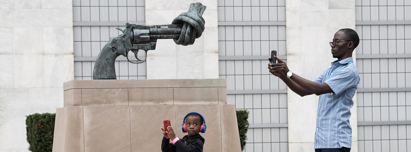 Un hombre y su hijo están parados junto a la escultura de una pistola con un cañón anudado tomando fotografías.