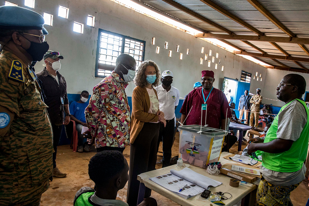 Military officers and civilians stand in front of a ballot box. 