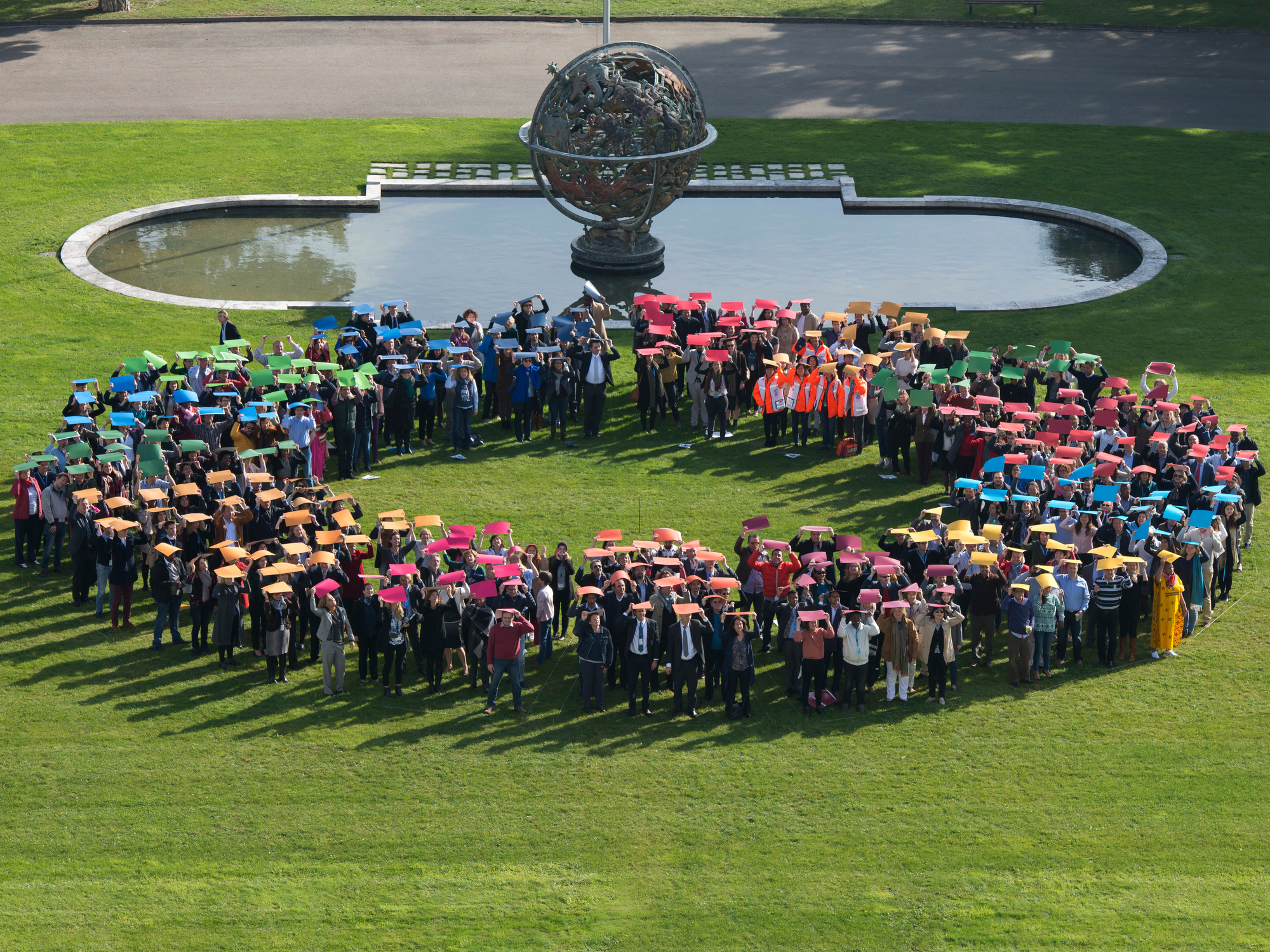 A large group of people form the outline of a circle holding up color boards to represent the SDGs logo.