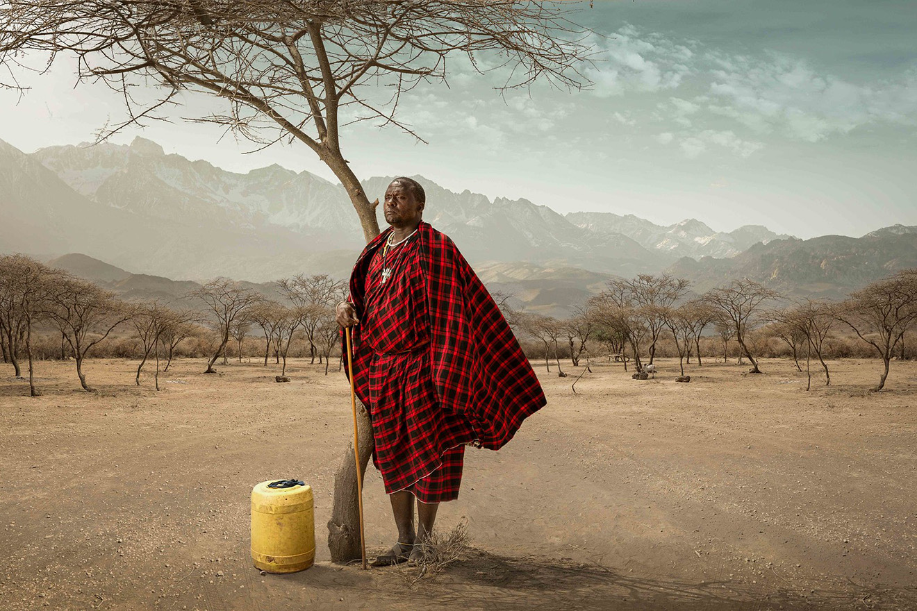 indigenous man standing next to tree and water container