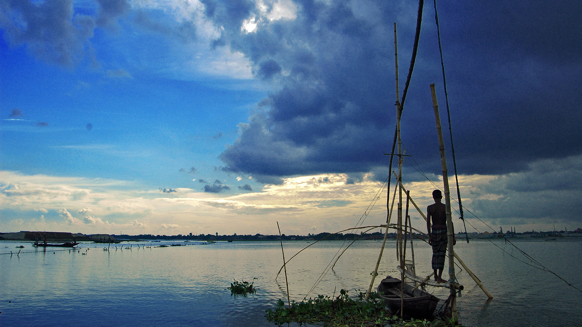 A fisherman at dusk stands above the water