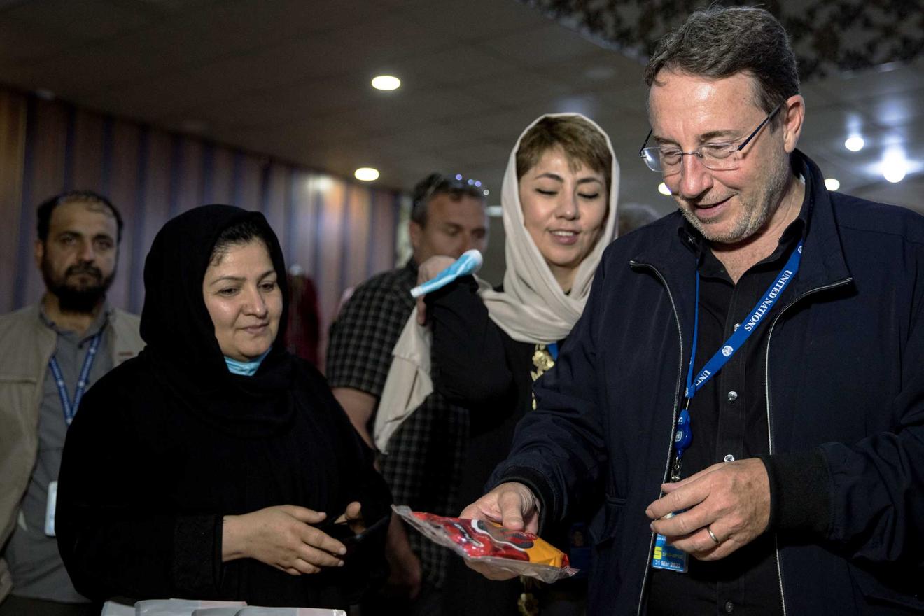 Achim looks at food packages with men and women standing next to him. The women wear veils.