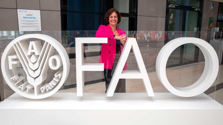 Beth stands behind an FAO sign in the outdoors