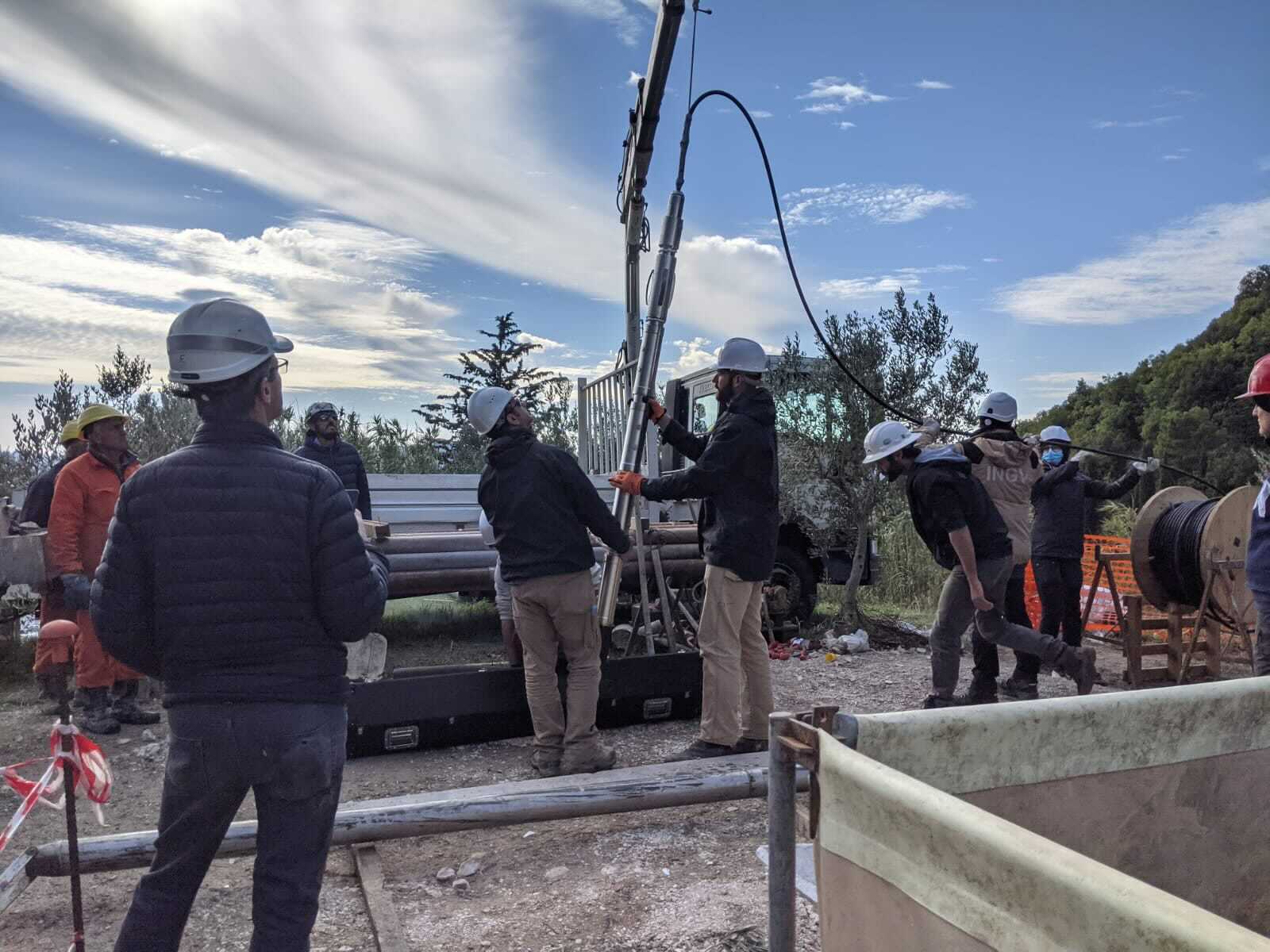 several people in hardhats lower long instrument into borehole