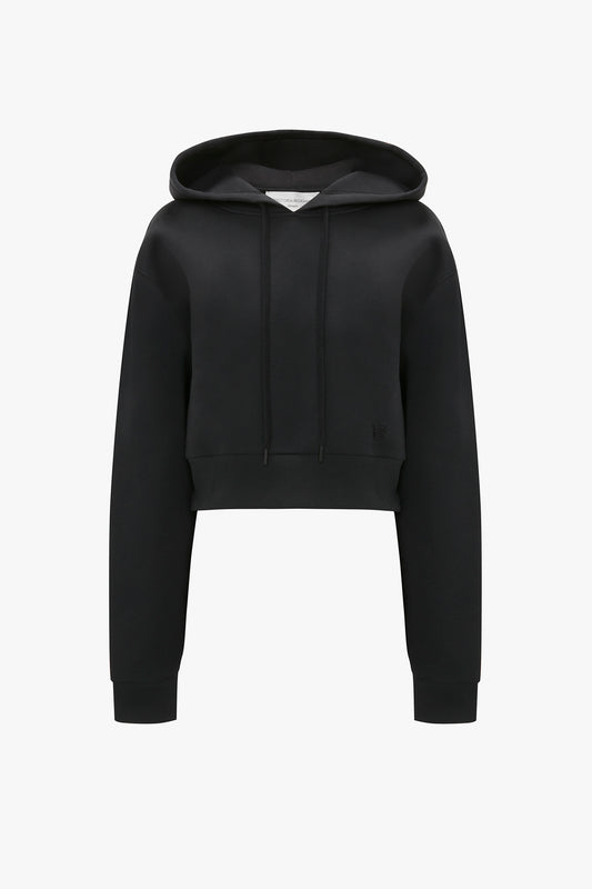 A Cropped Neoprene Hoodie In Black featuring a structured hood with a drawstring and long sleeves, along with the iconic Victoria Beckham monogram for added style.