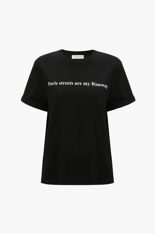 A black organic cotton T-shirt with rolled-up sleeves, featuring white text that reads, "Paris streets are my Runway," the PARIS STREETS ARE MY RUNWAY T-shirt in Black by Victoria Beckham.