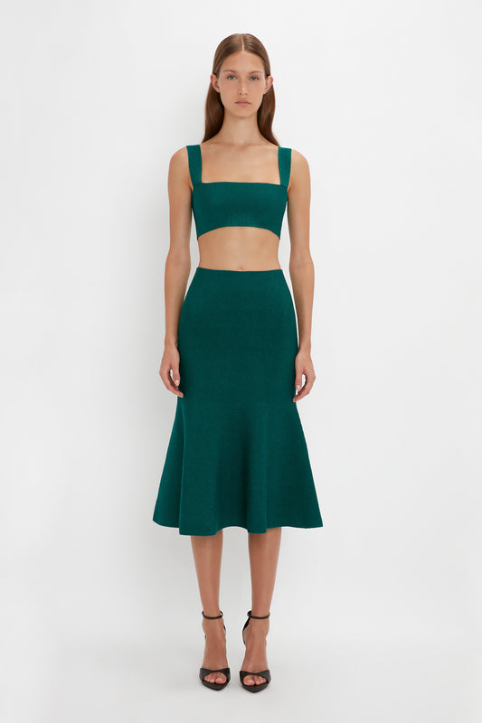 A person standing against a plain background wearing a green Victoria Beckham VB Body Strap Bandeau Top In Lurex Green with a flared skirt and black open-toe heels.