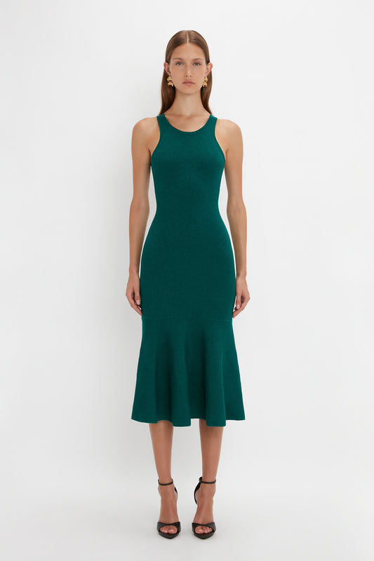 A woman stands against a white background, wearing a Victoria Beckham VB Body Sleeveless Dress In Lurex Green. The flattering flared silhouette enhances her figure, while her black high-heeled sandals add the perfect touch to this new-season wardrobe essential.