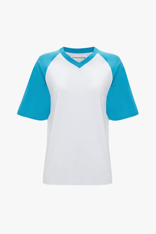 A white short-sleeve Exclusive Football T-Shirt In Blue with light blue raglan sleeves, a V-neck collar, and the stylish Victoria Beckham logo.