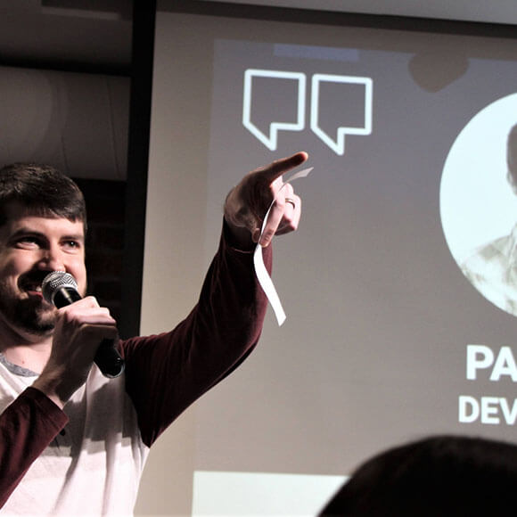 Man giving a presentation, pointing at a screen with speech bubble icons, holding a microphone.